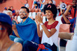 © Drazen - Happy black woman applauding while watching sports game at stadium.