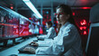woman in a lab coat working at a computer with multiple screens showing data and red lights in the background
