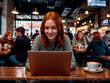 © Fabio Levy - Girl smiling and sitting at a table with a laptop and a cup of coffee. She is focused on her work. There are other people in the background, engaged in their own activities.