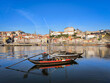 Navegando o Douro: Um barco Rabelo na ribeira de Vila Nova de Gaia, com a antiga cidade como pano de fundo