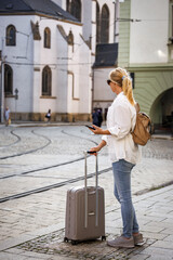 Wall Mural - Woman tourist with suitcase waiting for tram on street. Travel and public transportation in European city Olomouc, Czech Republic