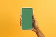 Modern bezel-less smartphone with blank green screen on hand isolated on yellow background