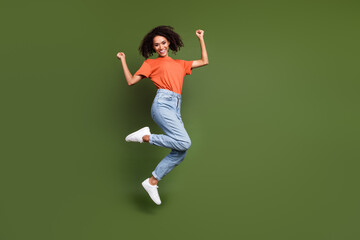 Wall Mural - Full length photo of pretty lucky lady dressed orange t-shirt jumping high rising fists empty space isolated khaki color background
