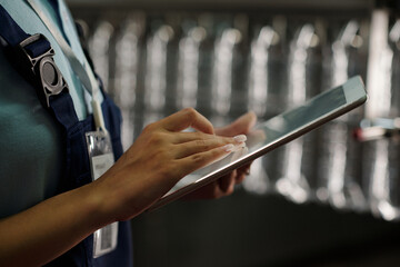 Poster - hand of young female engineer of factory scrolling on tablet screen against assembly line or conveyo