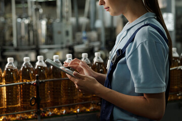 Poster - Tablet in hands of young quality inspector standing in front of line with capped plastic bottles with soda or lemonade in factory