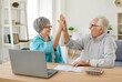 © Studio Romantic - Senior couple sitting at the table with laptop and bills giving high five each other calculating finances or taxes at home. Elderly retired man and woman rejoicing income and profit on pension.