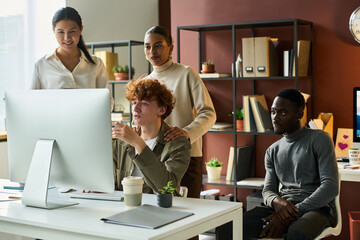 Leinwandbilder - Young confident male broker and group of his colleagues looking at computer screen during presentation of new project points