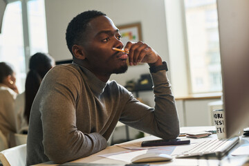 Poster - Young bored or tired male designer or broker with pencil by his mouth sitting in front of computer and looking at screen in office
