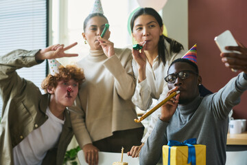 Poster - Young cheerful office workers in birthday caps whistling in noisemakers and looking at camera while one of them taking selfie