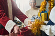 © pressmaster - Hands of young pregnant businesswoman taking giftbox with tied grey silk ribbon on top out of red sack held by Santa at xmas party