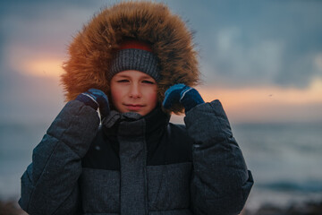 Canvas Print - Portrait of boy in winter jacket with hood on seashore in stormy weather