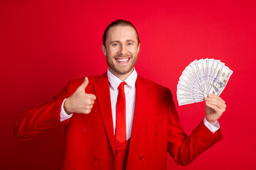 Canvas Print - Photo portrait of handsome young guy hold money fan show thumb up wear trendy classic outfit isolated on red color background