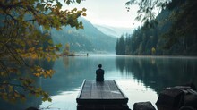 Person In Solitude On A Wooden Dock Overlooking A Calm Mountain Lake Surrounded By Autumn Foliage.