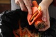 Woman peeling fresh carrot above garbage bin indoors, closeup