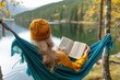 © Pinklife - A serene autumn day spent immersed in nature, as a woman sits by the tranquil lake, reading a book in her hammock under the shade of a tree
