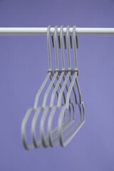 Wall Mural - Empty clothes hangers on rack against purple background, closeup