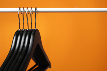 Wall Mural - Black clothes hangers on rack against orange background, closeup. Space for text