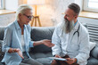 Senior male doctor examining his patient mature attractive woman during home or clinic visit. Healthcare for elderly retired people, insurance. Illness, disease diagnosis, treatment prescription