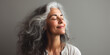 © piai - A gorgeous happy smiling senior woman with closed eyes and long grey hair over a grey background