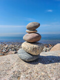 Fototapeta Tulipany - Tranquil Scene of a Stack of Smooth and Round Stones of Various Sizes Arranged on the Rocky Shore of a Calm Blue Lake, Set Against a Cloudless Sky Background in Bright Sunlight