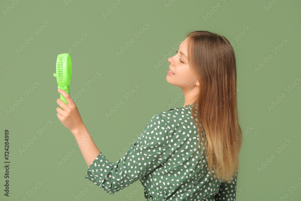 Beautiful young woman with handheld mini fan on green background