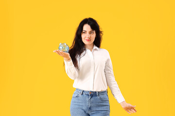 Young woman with piggy bank on yellow background