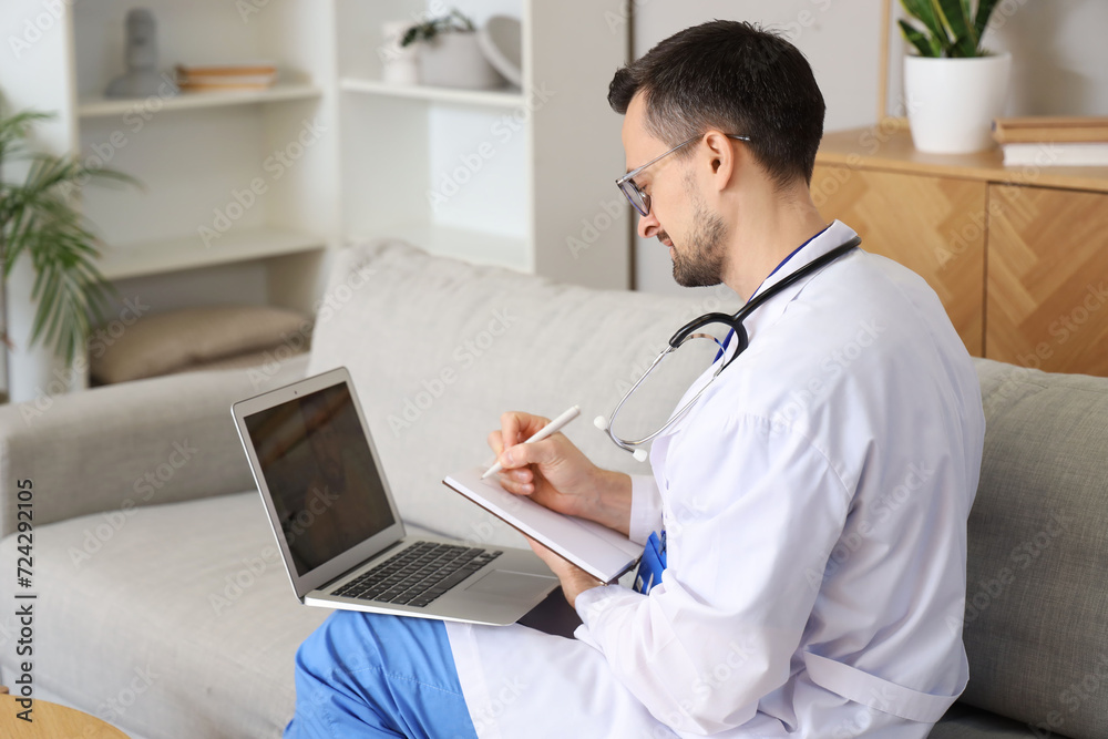 Handsome doctor video chatting with patient on laptop at home