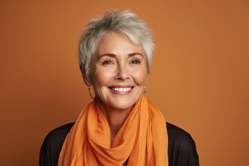 Portrait of smiling senior woman in orange scarf on orange background.