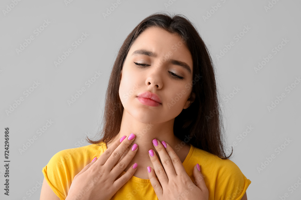 Young woman with thyroid gland problem on grey background