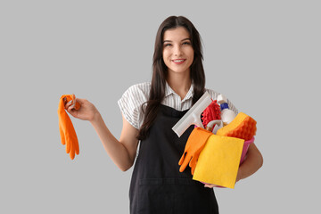 Wall Mural - Young woman with cleaning supplies on grey background