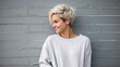 © red_orange_stock - Fashionable young woman with a chic short blonde haircut smiling against a gray brick wall.