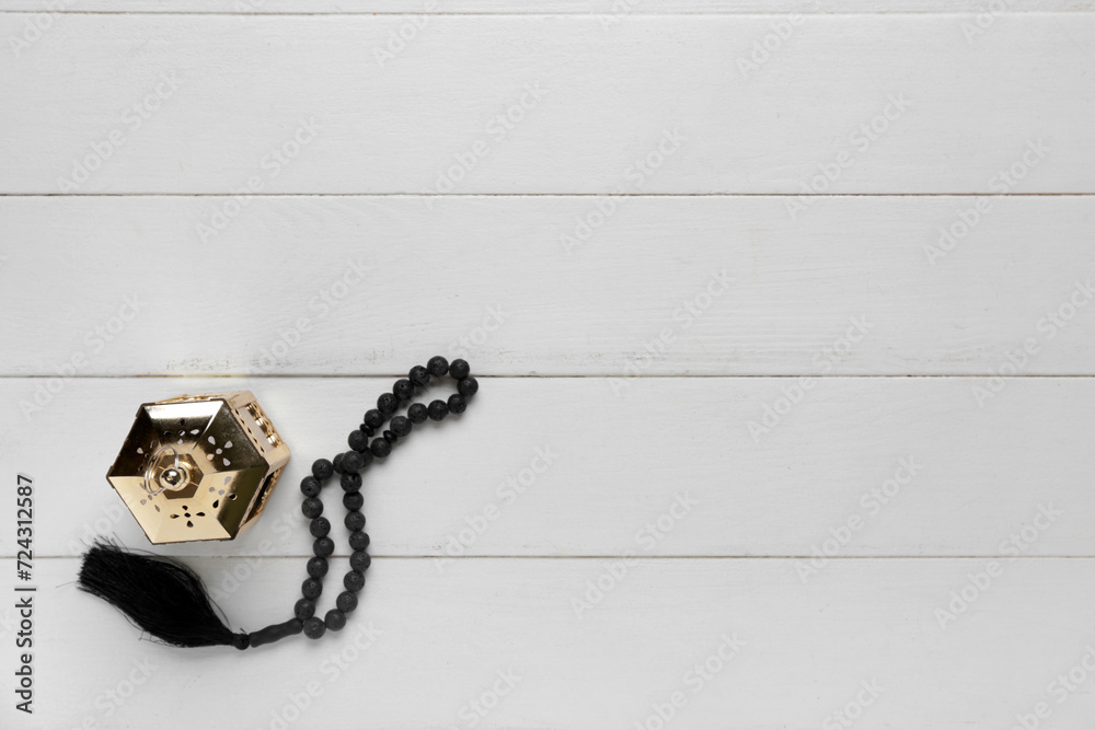Prayer beads and Muslim lantern for Ramadan on white wooden background