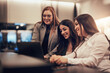© Flamingo Images - Smiling businesswomen working on a laptop together in a hotel lobby