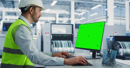Leinwandbilder - Caucasian Male Industrial Engineer In Hardhat Working on a Desktop Computer with Green Screen Chromakey on Display at an Electronics Factory Facility. Technological Research and Development Center.