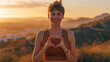 young woman is making a heart shape with her hands, smiling towards the camera with a beautiful sunset in the background