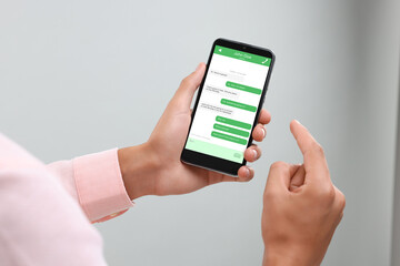 Man texting with friend using messaging application on smartphone against light grey background, closeup