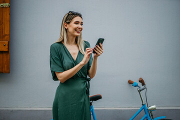 Beautiful female in a green summer dress, casually holding a bike and checking her phone