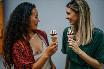 Two diverse female friends, one Chinese and one Caucasian, sharing laughter over ice cream in the vibrant city on a sunny summer day