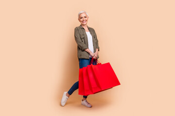 Sticker - Full body photo of attractive retired woman hold shopping bags dressed stylish khaki clothes isolated on beige color background