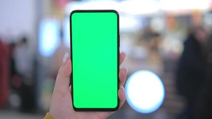 Use green screen for copy space closeup. Chroma key mock-up on smartphone in hand. Woman holds mobile phone and swipes photos or pictures in the mall 4K
