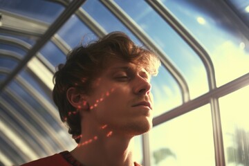Poster - A man with his eyes closed, standing by a window and gazing outside. This image can be used to depict contemplation, relaxation, or finding peace
