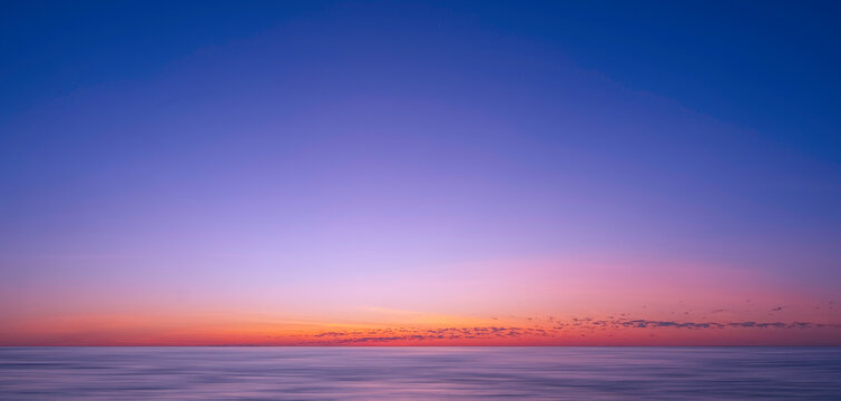 Idyllic natural sunrise sky background over sea in the early morning with motion blur of flowing water surface in panoramic view, beautiful tranquil seascape view in sunset time 