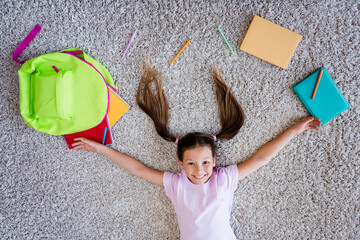 Poster - High angle view portrait of cheerful intelligent schoolchild lying comfy carpet floor backpack supplies house inside