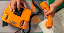 A Person Holding An Orange Telephone That Looks Like A Book