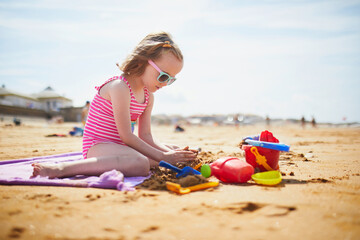 Wall Mural - Adorable preschooler girl playing on the sand beach at Atlantic coast of Brittany, France