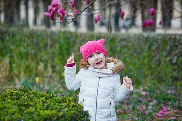 Wall Mural - Preschooler girl looking at pink magnolia in full bloom on a street of Paris, France