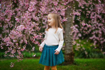 Wall Mural - Adorable preschooler girl enjoying nice spring day in park during cherry blossom season