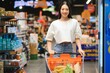 © Serhii - Happy young woman looking at product at grocery store. Smiling woman shopping in supermarket