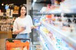 © Serhii - Young smiling happy woman 20s in casual clothes shopping at supermaket store with grocery cart