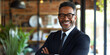 © J. Grayscale - Charismatic African American executive in a sharp suit, standing in a bright workspace
